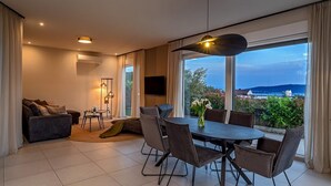 Een moderne woonkamer met een eethoek, grote ramen en uitzicht op zee.