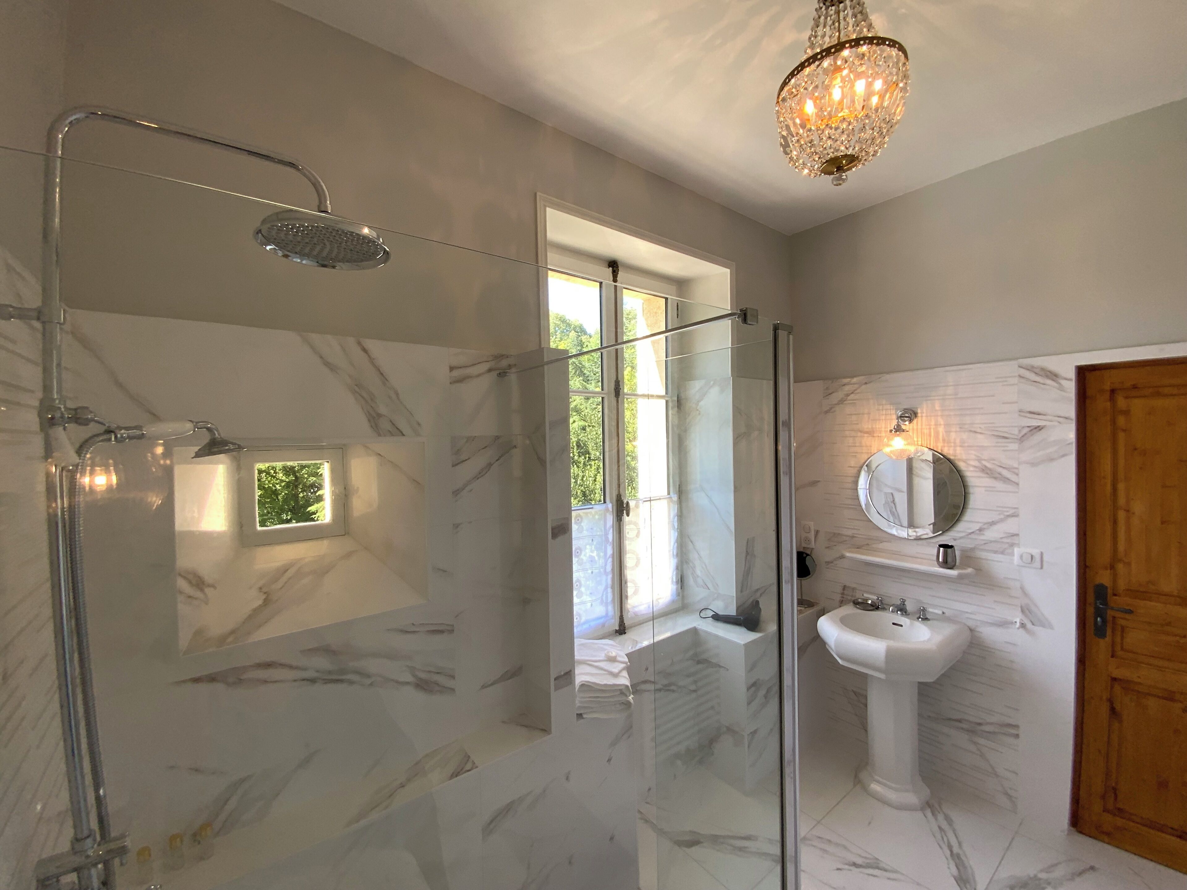 Une salle de bain moderne avec une douche à parois de verre, un lavabo sur colonne et un lustre.