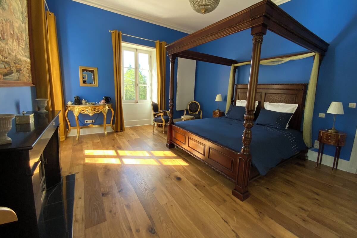 Una cama con dosel, un escritorio de madera, una silla y una mesita de noche con una lámpara.