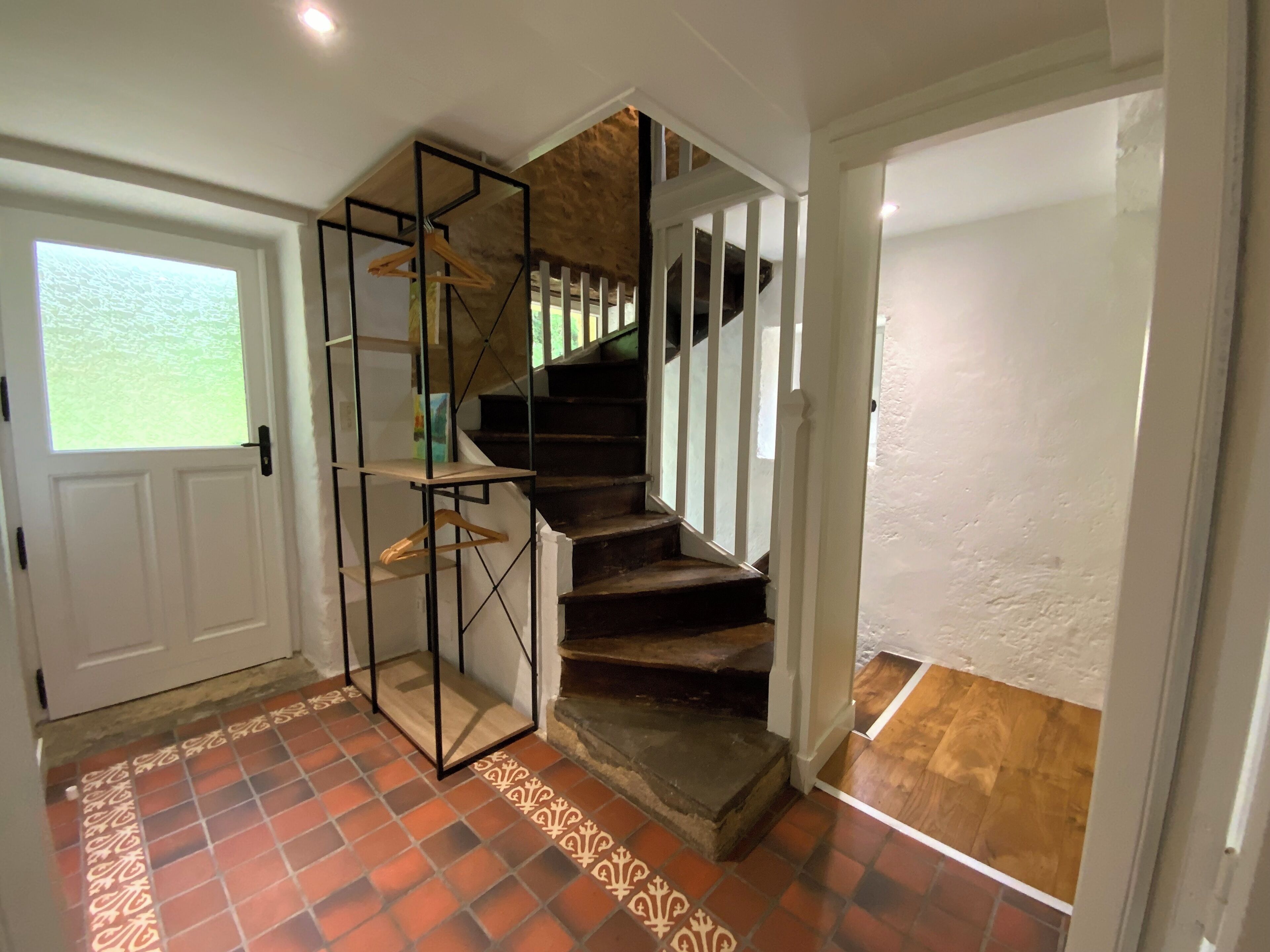 Una escalera con acabado de madera y barandales blancos, que conduce a una habitación con piso de baldosas y una puerta con ventanal.