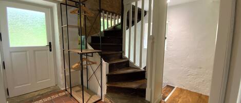 Una escalera con acabado de madera y barandales blancos, que conduce a una habitación con piso de baldosas y una puerta con ventanal.