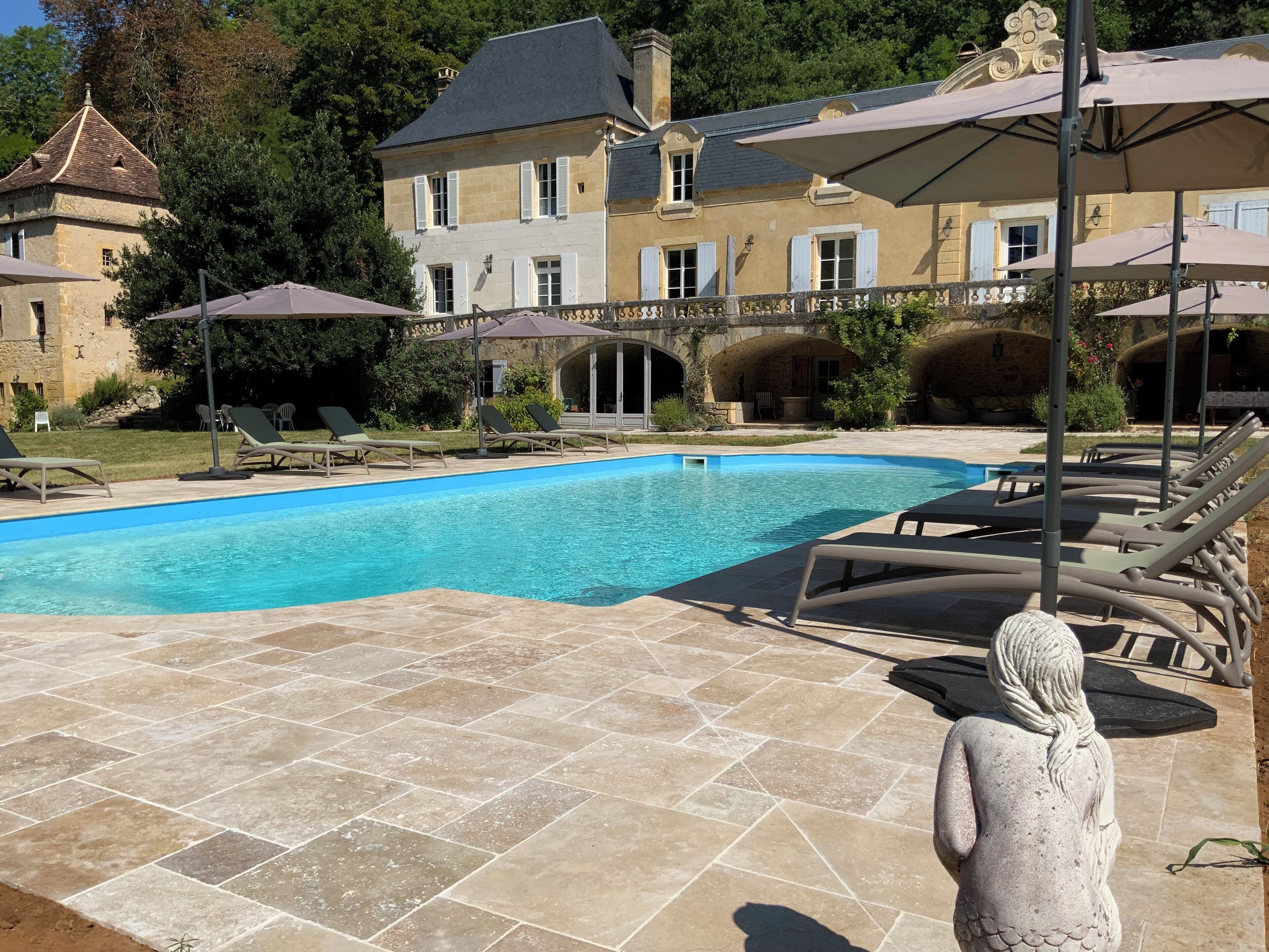 Ein Swimmingpool mit Liegestühlen und Sonnenschirmen, umgeben von einer Steinterrasse.