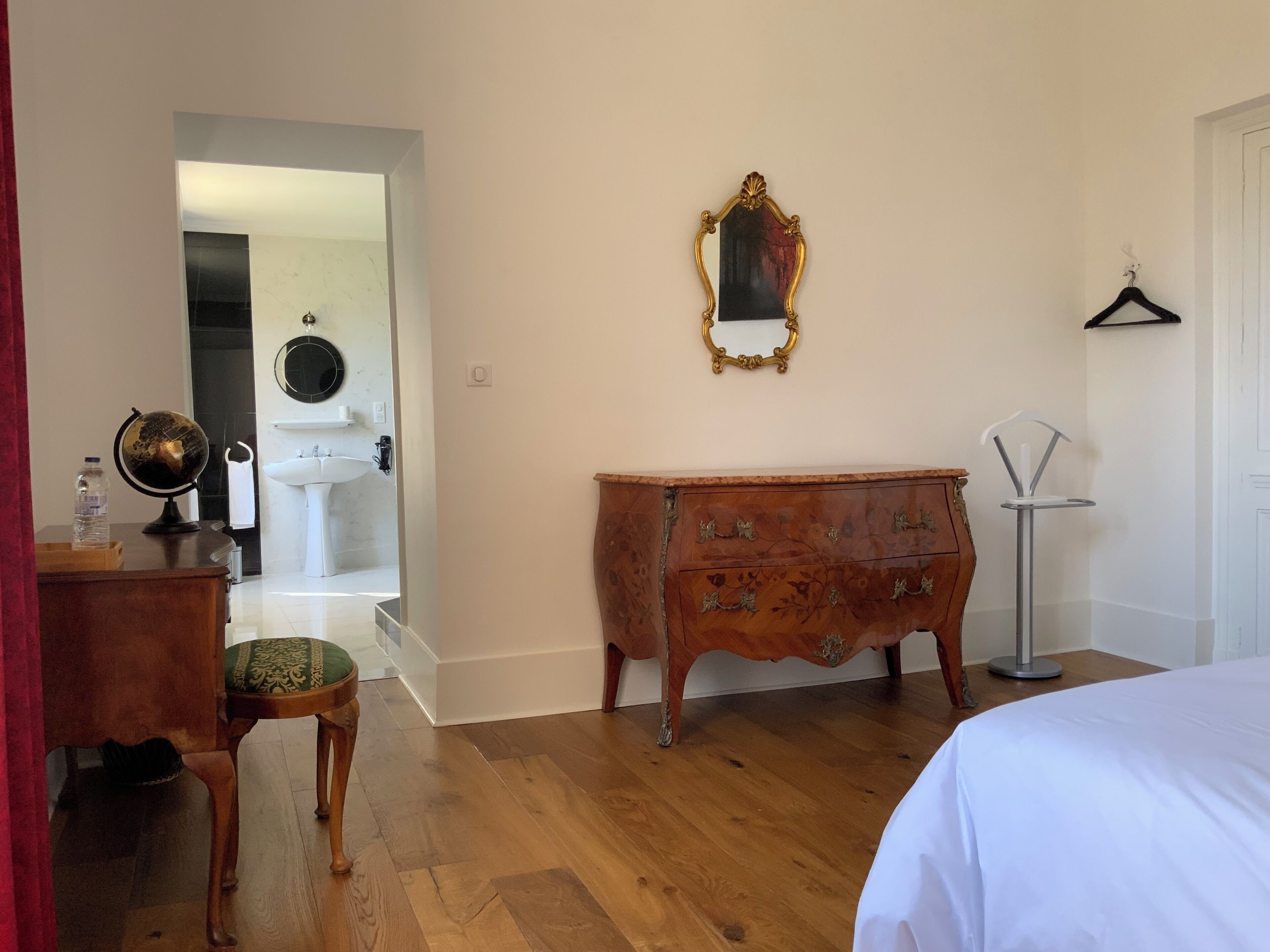 Una habitación con tocador de madera, cama, globo terráqueo y espejo en la pared.