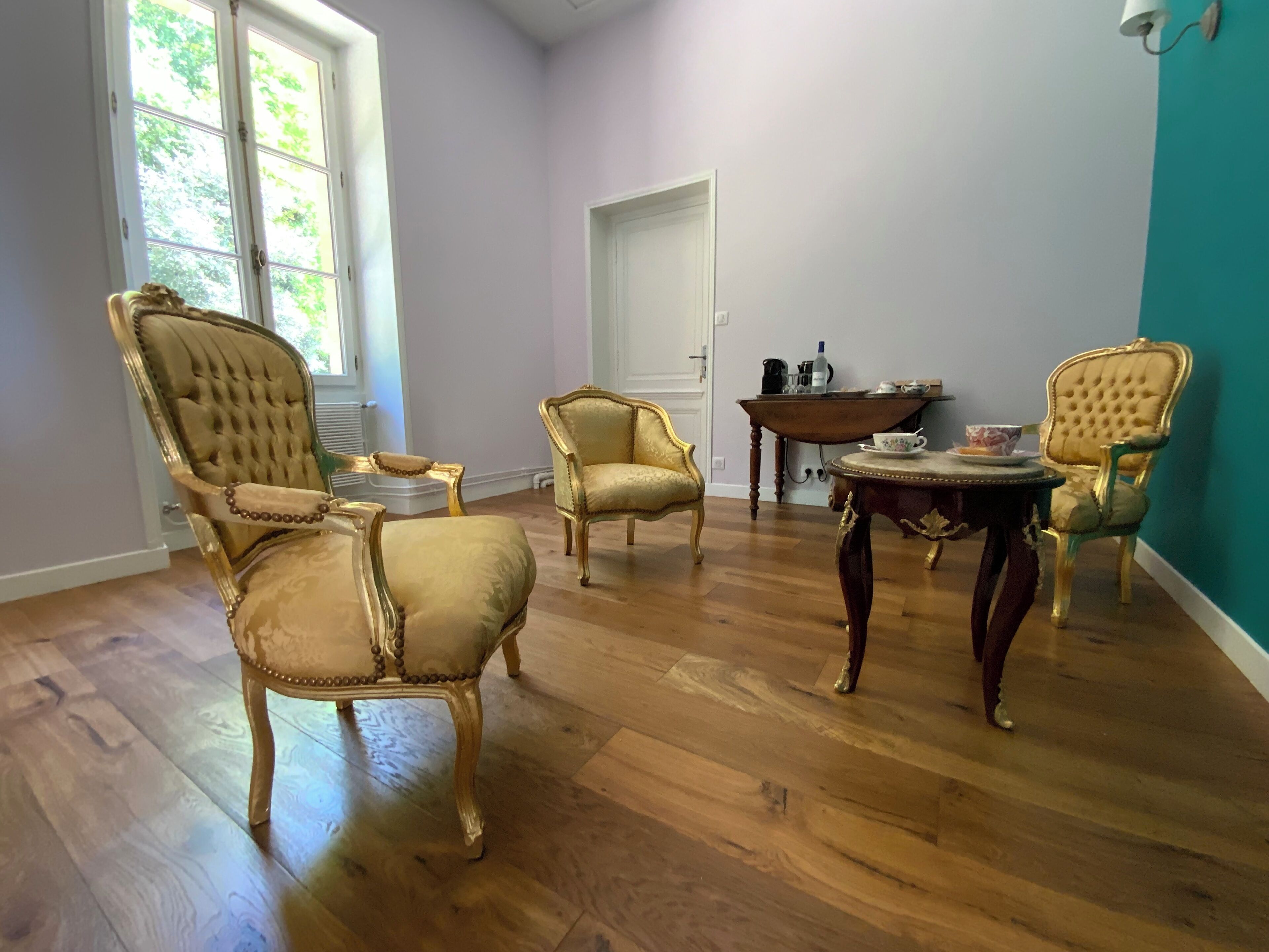 Une pièce avec un plancher en bois, une porte blanche et trois fauteuils rembourrés ornés de bordures dorées.