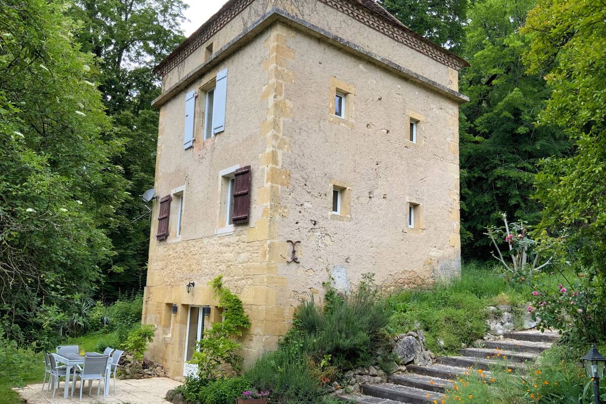 Un edificio de piedra con jardín, asientos al aire libre y una escalera que lo lleva a la entrada.