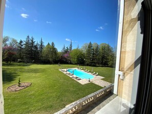 Vue d’une cour arrière avec une piscine, entourée d’une pelouse bien entretenue et d’arbres.