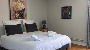 Una cama bien hecha con sábanas blancas, cabecera oscura y un retrato enmarcado en la pared.