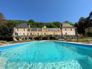 Une grande piscine avec un pont de pierre menant à un bâtiment historique doté de plusieurs arcades.