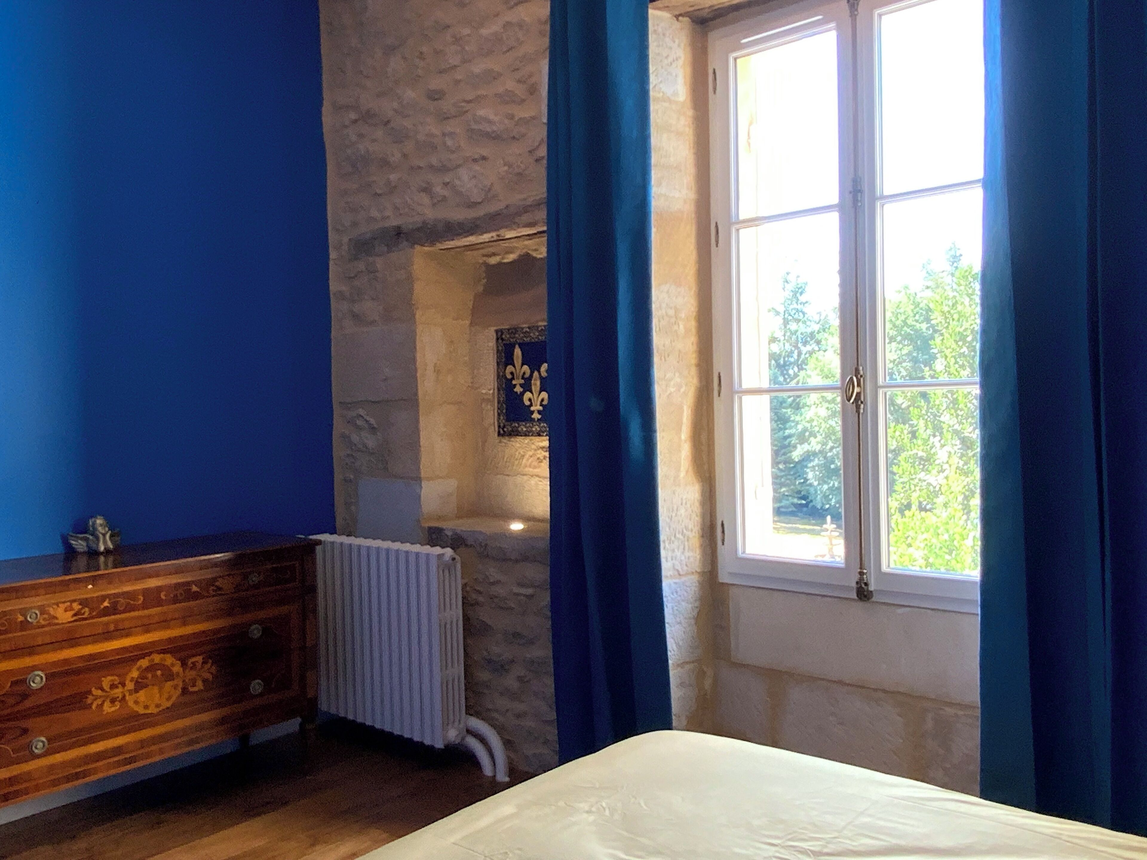 Una camera da letto con una parete in pietra, un comò in legno, un termosifone e una finestra con tende.