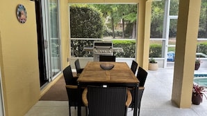 Un porche cubierto con una mesa y sillas de madera, una parrilla y vistas al verdor.
