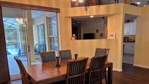 Un comedor con una mesa y sillas de madera, una cocina al fondo y vistas a través de un ventanal.