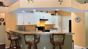 Una cocina con armarios blancos, una isla central con taburetes y un reloj en la pared.