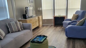 Un salon avec un canapé gris, un fauteuil bleu, un pouf vert et un meuble en bois.