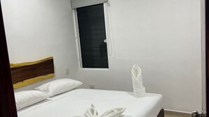 Et hotelværelse med en seng, et vindue med persienne, en aircondition samt et håndklæde på sengen.