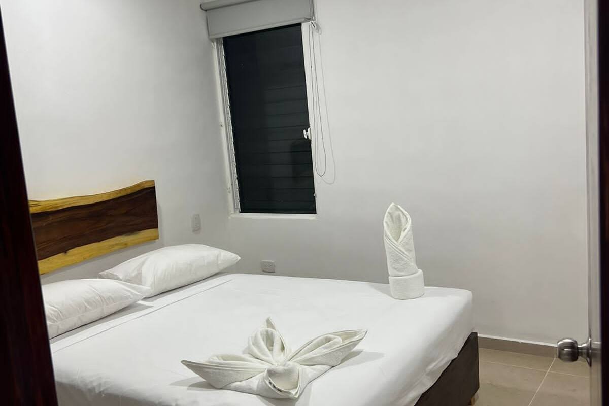 A hotel room with a bed, a window with a blind, an air conditioning unit, and a towel on the bed.