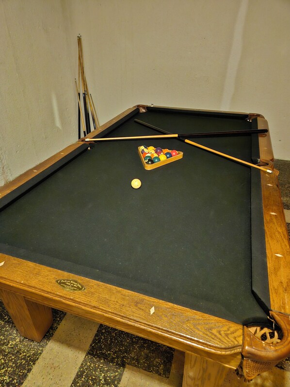 Ein Billardtisch mit einem Queue, einer Kugelaufbewahrung und einem Billardball auf der Spielfläche.