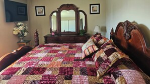 Une chambre à coucher avec un grand lit, une commode, un miroir et un téléviseur fixé au mur.