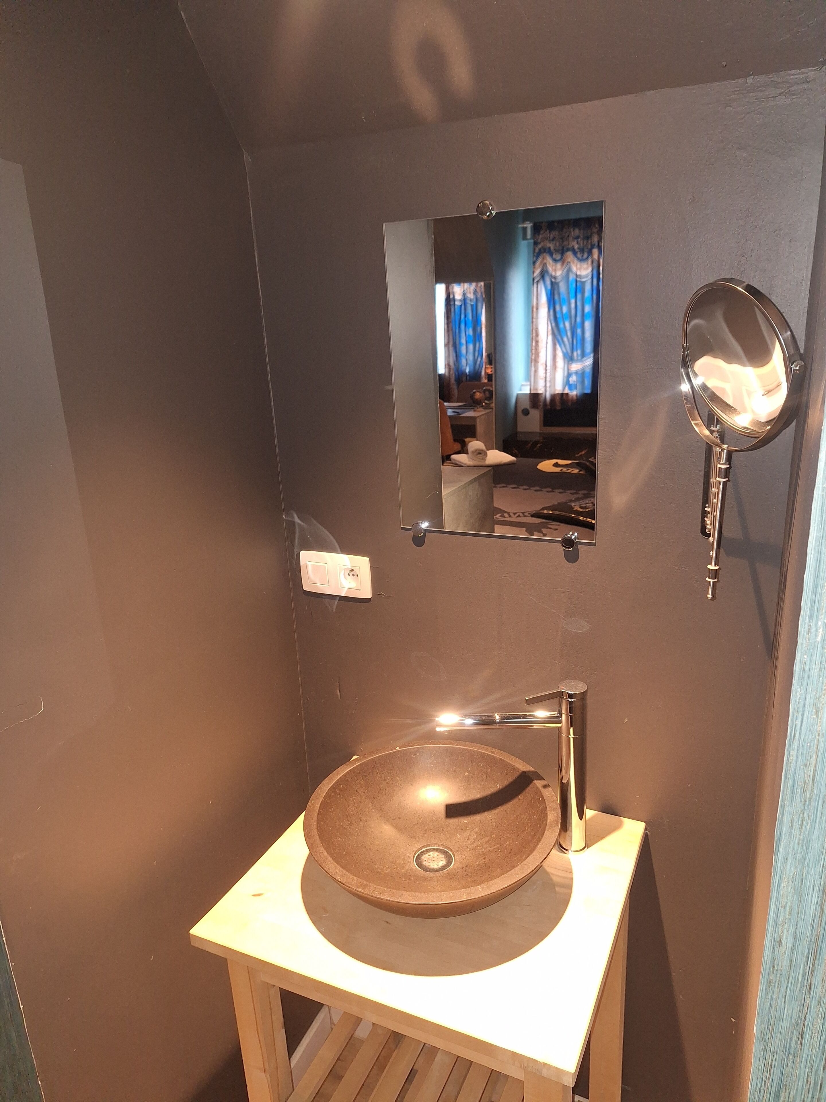 A bathroom with a round vessel sink, a mirror, and a small window with curtains.