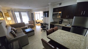 A compact living space with a kitchenette, a dining area, and a seating area with a sofa and ottoman.