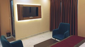 A hotel room with a flat-screen TV mounted on the wall, two blue armchairs, a red bedspread, and a marble floor. - Hotel Shivalayam (Varanasi)