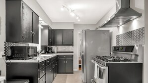 Une cuisine moderne avec des meubles de couleur sombre, des appareils électroménagers en acier inoxydable et un dosseret carrelé.
