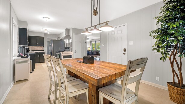 Une cuisine moderne avec des meubles blancs, une table à manger en bois et un luminaire suspendu.