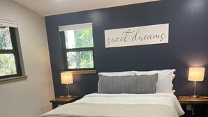 A bedroom with a bed, two bedside tables, a bench, a wall sign, and a window. - Quiet, Creekside Home with Rain Spa Shower, Unplug & Relax (Collins)