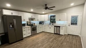 A modern kitchen with white cabinets, a stainless steel refrigerator, an oven, and a dishwasher. - Quiet, Creekside Home with Rain Spa Shower, Unplug & Relax (Collins)