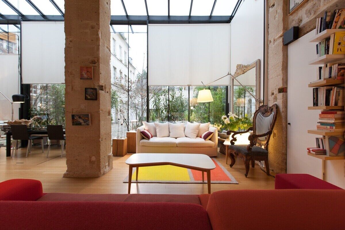 A spacious living room with a large window, a sofa, a coffee table, and a bookshelf.