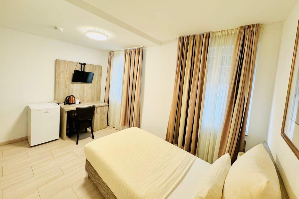 A hotel room with a bed, a desk, a television, and curtains.