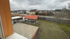 A view from a window overlooking a courtyard with a red-roofed pavilion, a paved area, and a fence. - Hotel Soad (Salach)