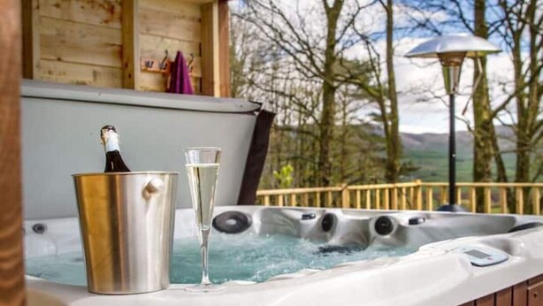 A hot tub with champagne and a glass, surrounded by wooden deck and trees. - Stunning Character Property with Hot tub (kendal)