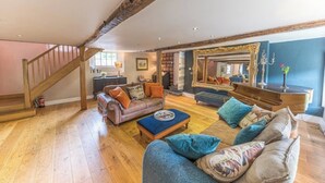 A spacious living room with a wooden staircase, a large mirror, and a cozy seating area with a sofa and armchairs. - Stunning Character Property with Hot tub (kendal)