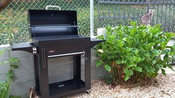 A barbecue grill with a closed lid, surrounded by greenery and a fence.