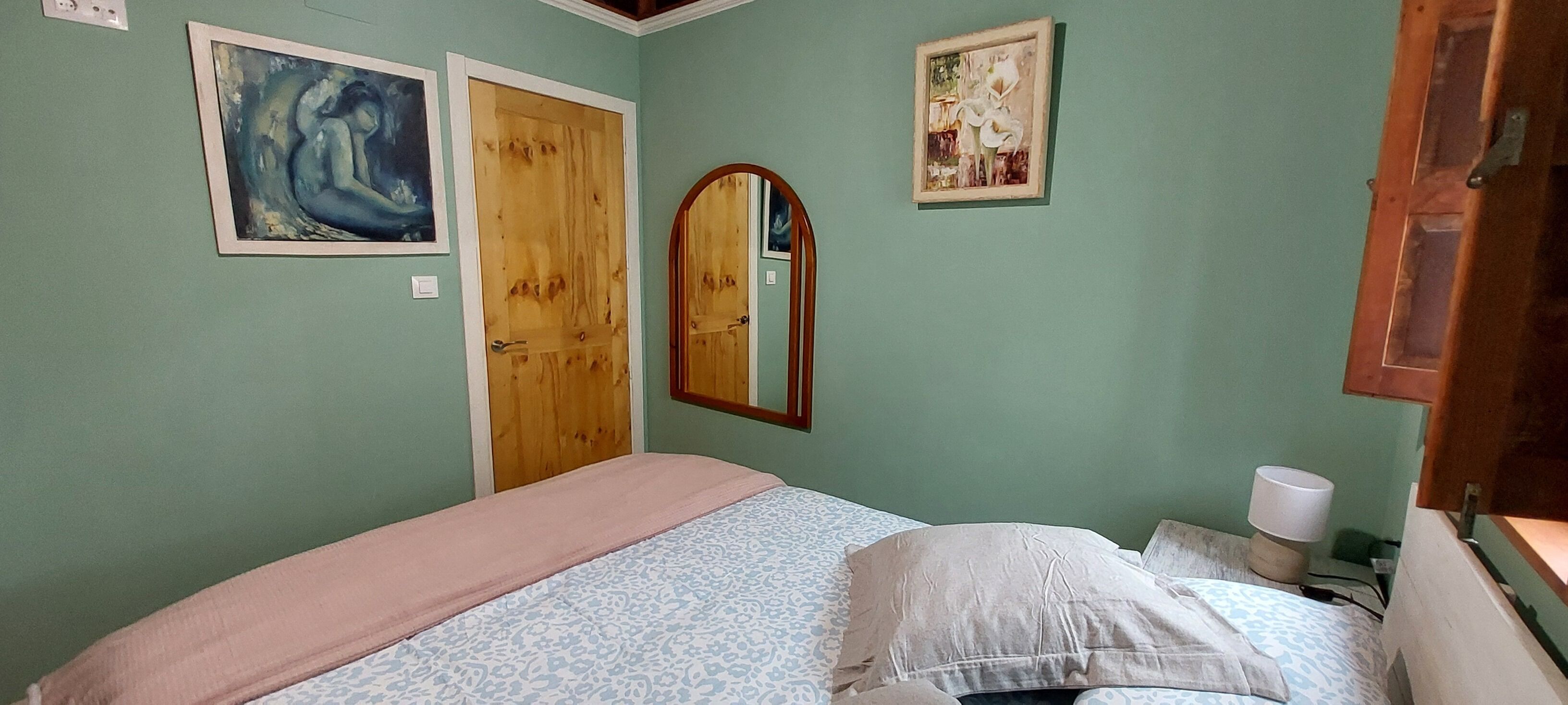 Ein Schlafzimmer mit einem Bett, einer Holztür, einem Spiegel und zwei gerahmten Kunstwerken an der Wand.
