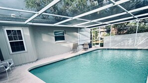 Una piscina con zona techada, ventana y un pequeño espacio de descanso con sillas.