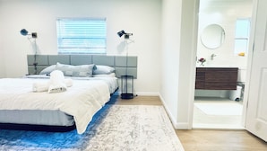 Un dormitorio moderno con una cama grande, dos lámparas de noche, una mesita de noche y vistas al baño.