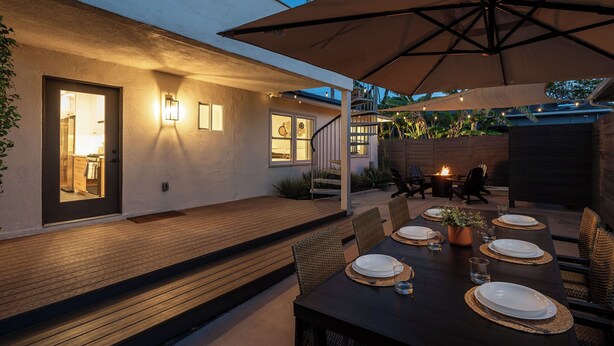 An outdoor dining area with a wooden deck, a table set for four, and a large umbrella providing shade.