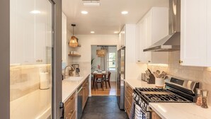 A modern kitchen with white cabinets, a stainless steel stove, and a dining area with a table and chairs.