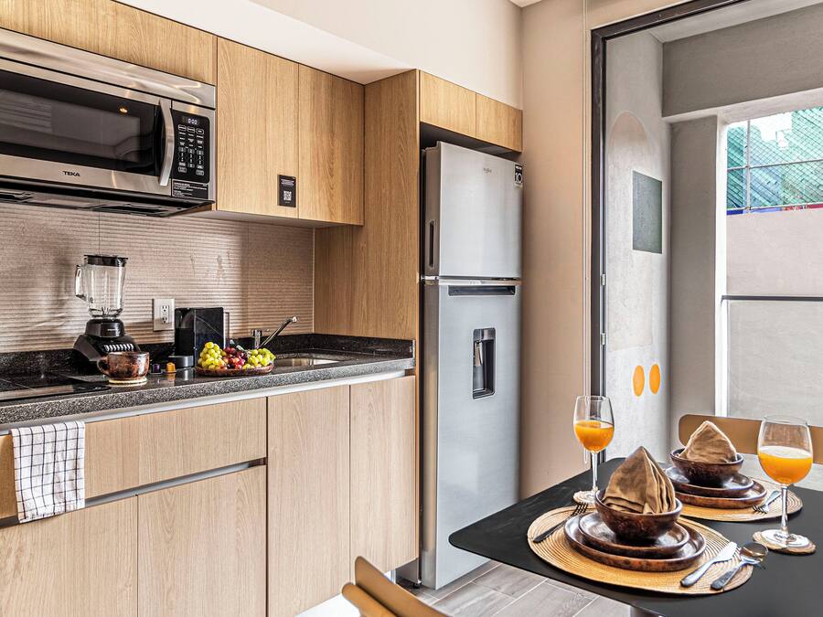 Uma cozinha moderna com micro-ondas embutido, frigorífico e área de jantar com uma mesa posta para dois.