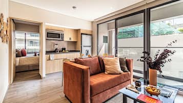 Una sala de estar moderna con un sofá, una mesa de centro y vistas a una cocina a través de un ventanal.
