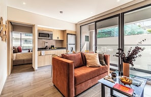 Una sala de estar moderna con un sofá, una mesa de centro y vistas a una cocina a través de un ventanal.