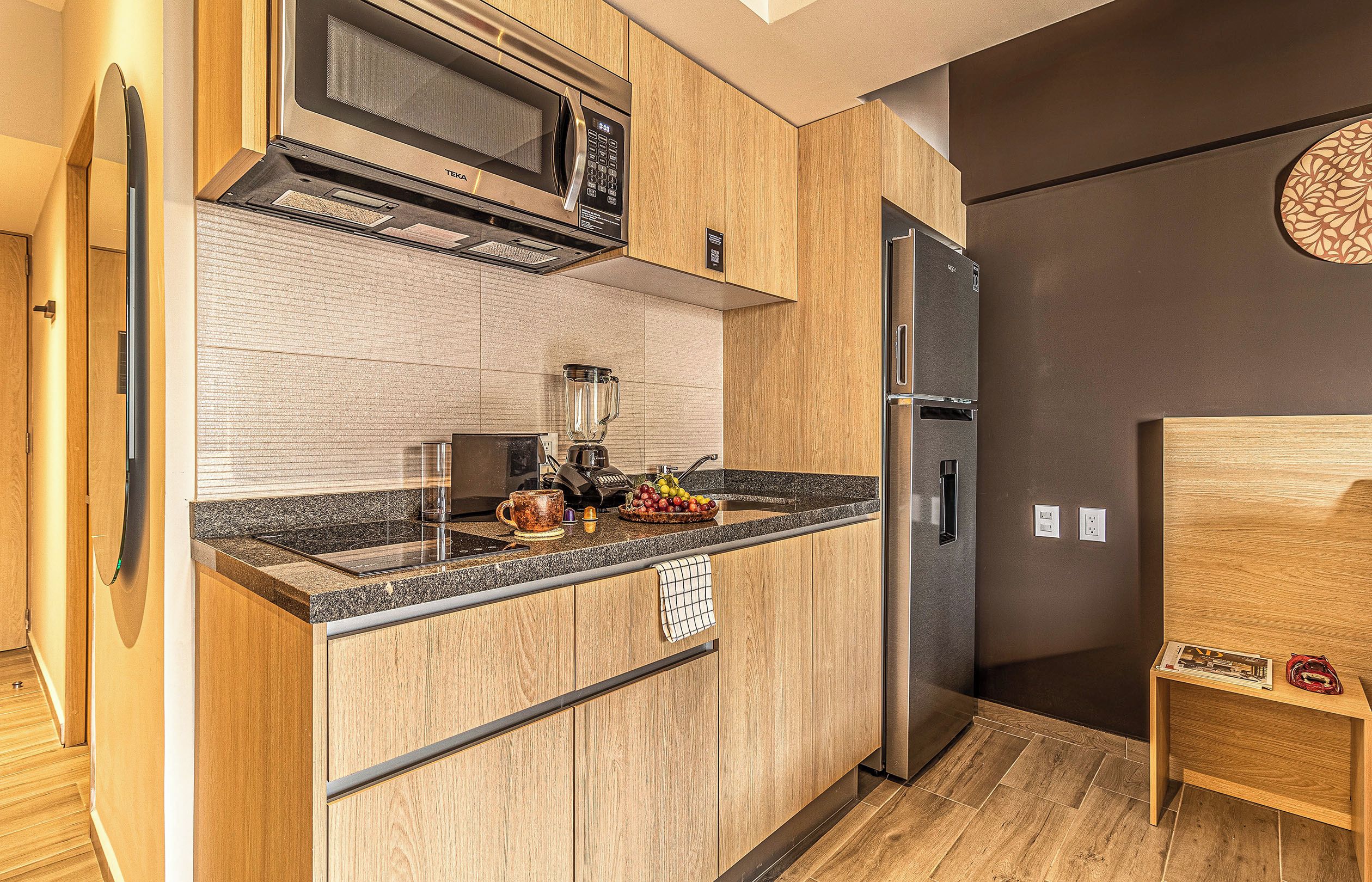A modern kitchen with a built-in microwave, a refrigerator, and a countertop with a blender and fruit.