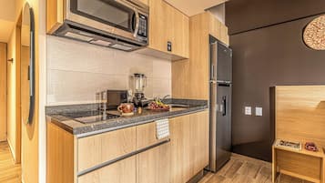 Une cuisine moderne équipée d’un four à micro-ondes encastré, d’un réfrigérateur et d’un plan de travail sur lequel se trouvent un mixeur et des fruits.