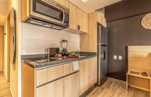 Una cocina moderna con microondas integrado, refrigerador y encimera con batidora y fruta.