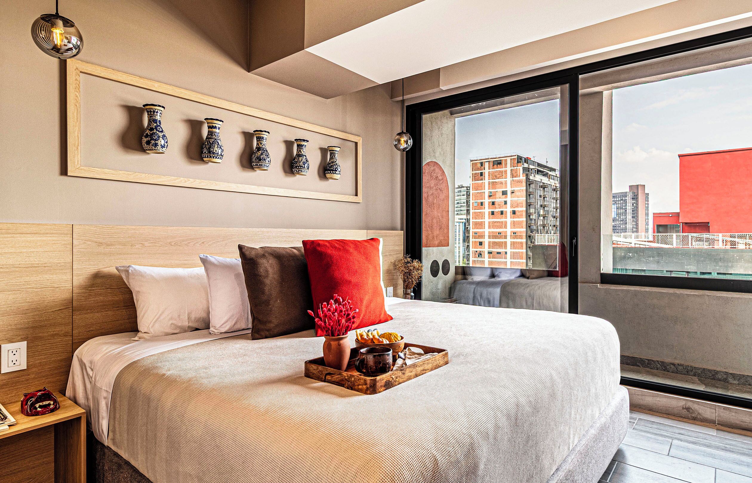 Moderni hotellihuone, jossa on suuri sänky, näköala kaupunkiin ja seinällä oleva kehystetty maljakkojen kokoelma.