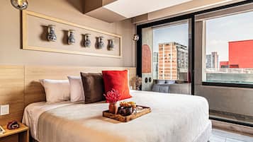 Moderni hotellihuone, jossa on suuri sänky, näköala kaupunkiin ja seinällä oleva kehystetty maljakkojen kokoelma.