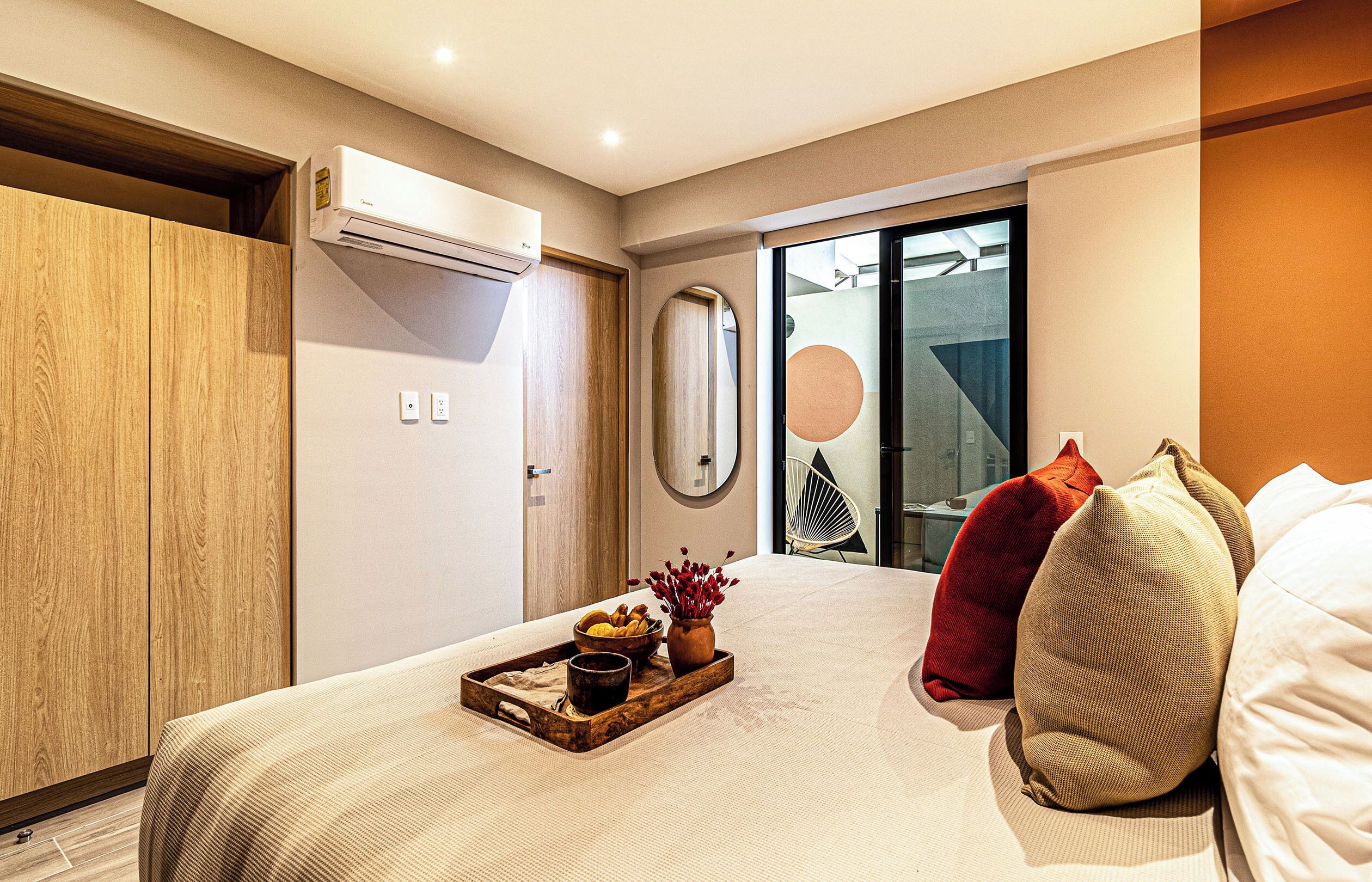 Habitación de hotel con cama, armario de madera, equipo de aire acondicionado, espejo y vistas al exterior a través de una puerta de cristal.