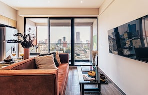 A modern living room with a sofa, a coffee table, and a city view through large windows.