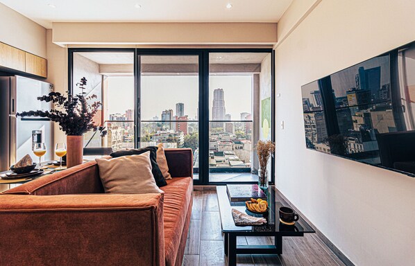 Uma sala de estar moderna com um sofá, uma mesa de centro e vista para a cidade através de grandes janelas.